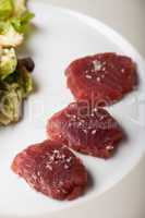 drei Scheiben rohen Tunfischs mit Salz und Salat