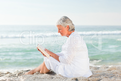 Elderly woman reading her book on the beach