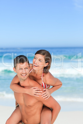 Handsome man having wife a piggyback on the beach