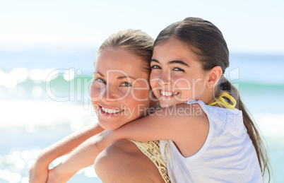 Mother having daughter a piggyback at the beach