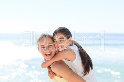 Mother having daughter a piggyback at the beach