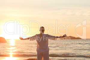 Woman practicing yoga during the sunset at the beach