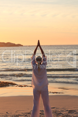 Woman practicing yoga during the sunset at the beach