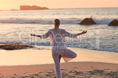 Woman practicing yoga during the sunset at the beach