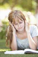 Female Teenage Student Studying In Park Looking Puzzled