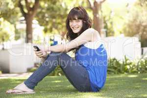 Portrait Of  Teenage Girl Sitting In Park Using Mobile Phone