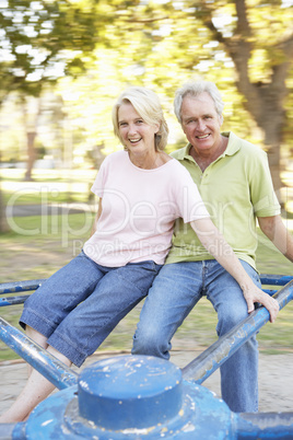 Senior Couple Riding On Roundabout In Park