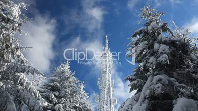 Cellular tower in snow on a blue sky background with clouds passing by