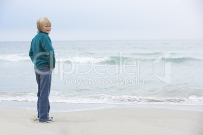 Young Boy On Holiday Standing On Winter Beach Looking Out To Sea