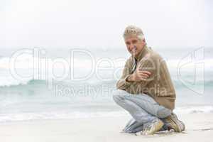 Senior Man On Holiday Kneeling On Winter Beach