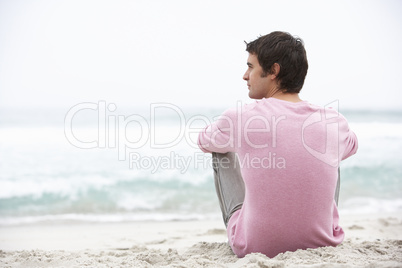 Young Man On Holiday Sitting On Winter Beach