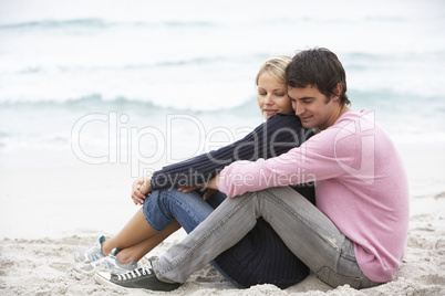 Young Couple On Holiday Sitting On Winter Beach