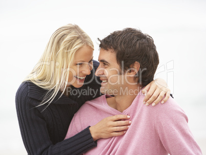 Young Couple On Holiday Sitting On Winter Beach