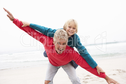 Grandfather Giving Grandson Piggy Back On Winter Beach