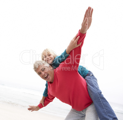 Grandfather Giving Grandson Piggy Back On Winter Beach