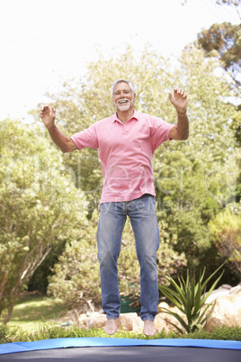 Senior Man Jumping On Trampoline In Garden