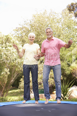 Senior Couple Jumping On Trampoline In Garden