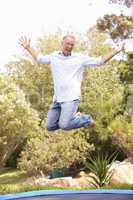 Middle Aged Man Jumping On Trampoline In Garden