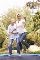 Couple Jumping On Trampoline In Garden