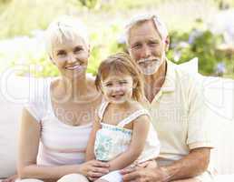 Grandparents And Granddaughter Relaxing In Garden