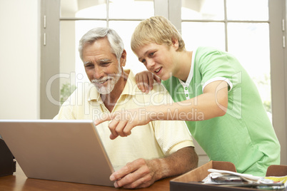 Teenage Grandson Helping Grandfather To Use Laptop At Home