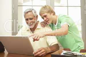 Teenage Grandson Helping Grandfather To Use Laptop At Home