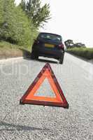 Car Broken Down On Country Road With Hazard Warning Sign In Fore