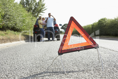 Family Broken Down On Country Road With Hazard Warning Sign In F