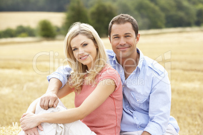 Couple Sitting On Straw Bales In Harvested Field