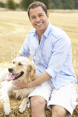 Man Sitting With Dog On Straw Bales In Harvested Field