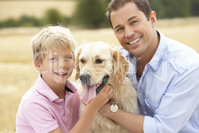 Father And Son Sitting With Dog On Straw Bales In Harvested Fiel