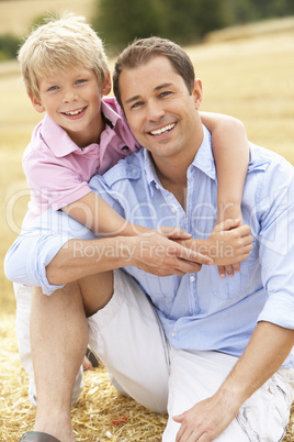 Father And Son Sitting On Straw Bales In Harvested Field
