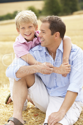 Father And Son Sitting On Straw Bales In Harvested Field