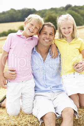 Father And Children Sitting On Straw Bales In Harvested Field