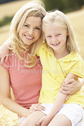 Mother And Daughter Sitting On Straw Bales In Harvested Field