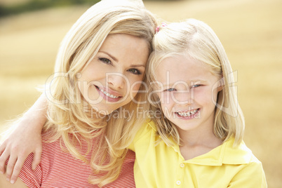 Mother And Daughter Sitting On Straw Bales In Harvested Field