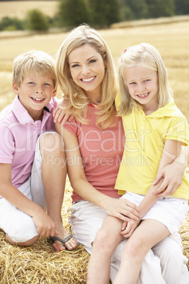 Mother And Children Sitting On Straw Bales In Harvested Field