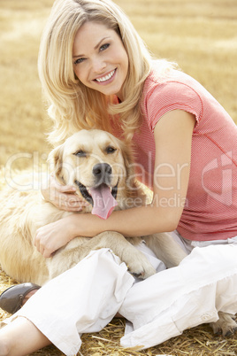 Woman Sitting With Dog On Straw Bales In Harvested Field