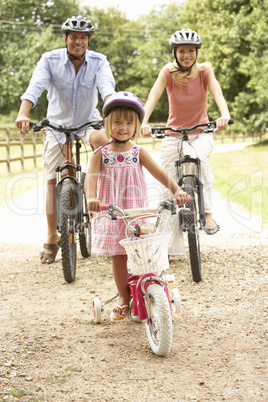 Family Cycling In Countryside Wearing Safety Helmets