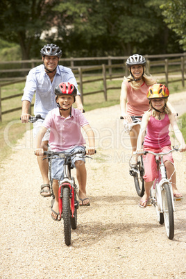 Family Cycling In Countryside Wearing Safety Helmets