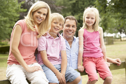 Portrait Of Family Sitting On Fence In Countryside