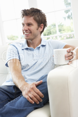 Man Sitting On Sofa Drinking Coffee Relaxing At Home