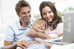 Family Sitting On Sofa Using Laptop At Home