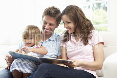 Family Sitting On Sofa Reading Book At Home