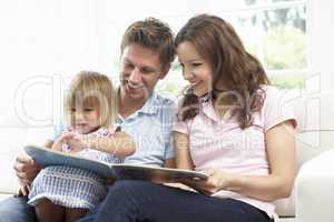 Family Sitting On Sofa Reading Book At Home