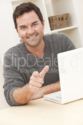 Smiling Man Using Laptop Computer At Home Pointing To Camera