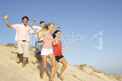 Group Of Friends Enjoying Beach Holiday Running Down Dunes