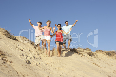 Group Of Friends Enjoying Beach Holiday Running Down Dunes