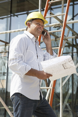 Architect With Plans Outside New Home Talking On Mobile Phone