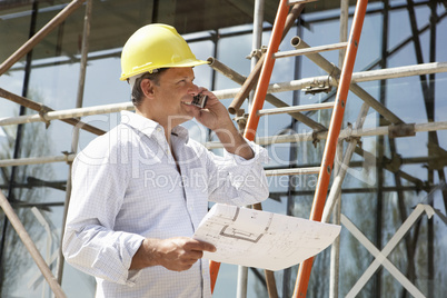 Architect With Plans Outside New Home Talking On Mobile Phone